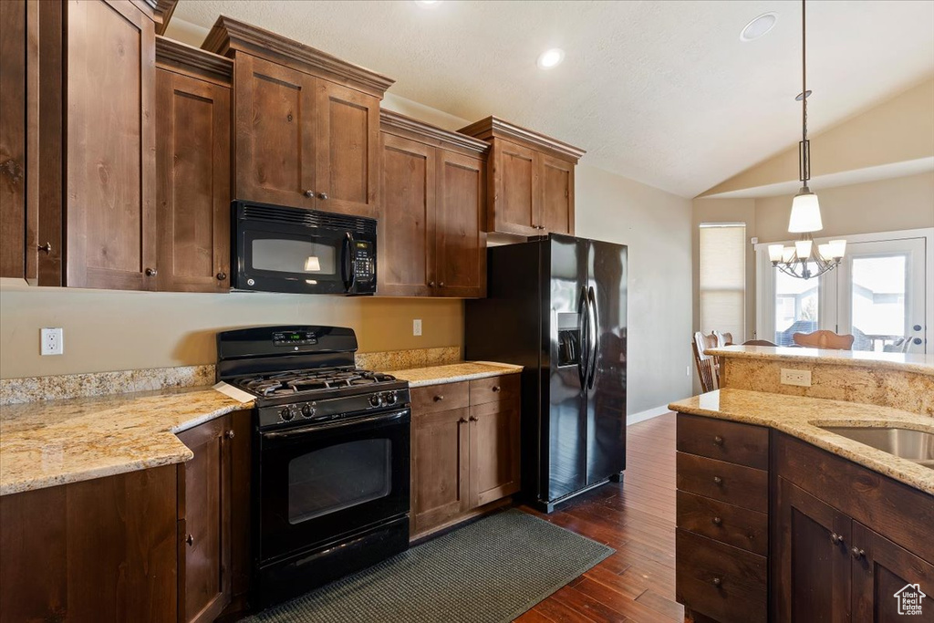 Kitchen featuring black appliances, dark wood finished floors, vaulted ceiling, hanging light fixtures, and light stone countertops