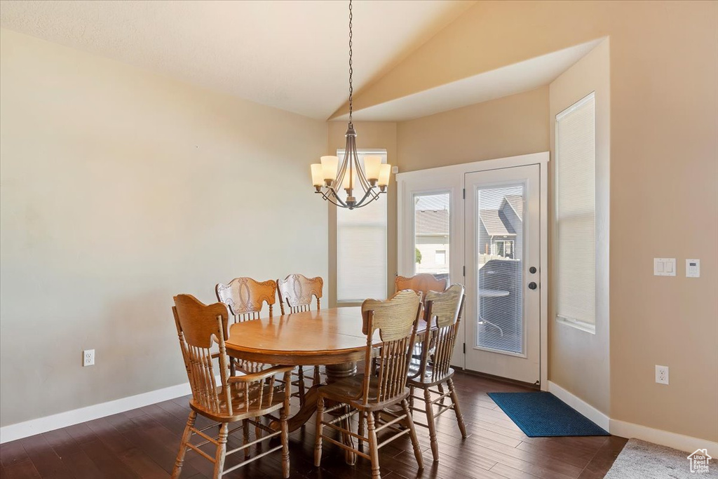 Dining area with a chandelier, vaulted ceiling, dark wood-style flooring, and baseboards