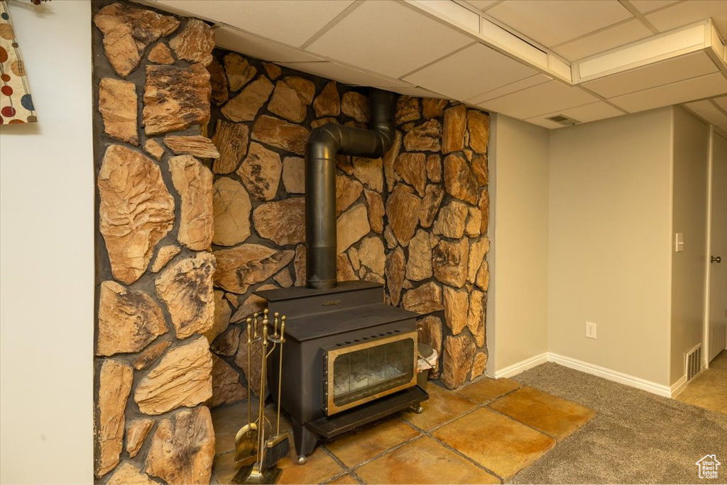 Detailed view of carpet flooring, a wood stove, a drop ceiling, and baseboards