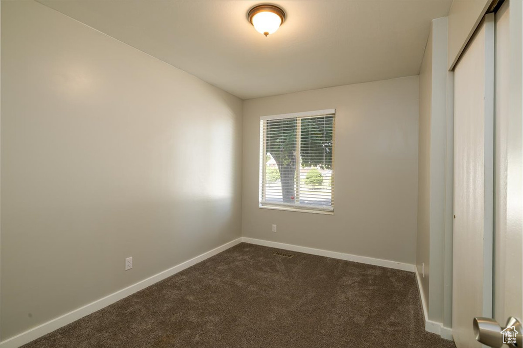 Unfurnished room featuring dark colored carpet and baseboards