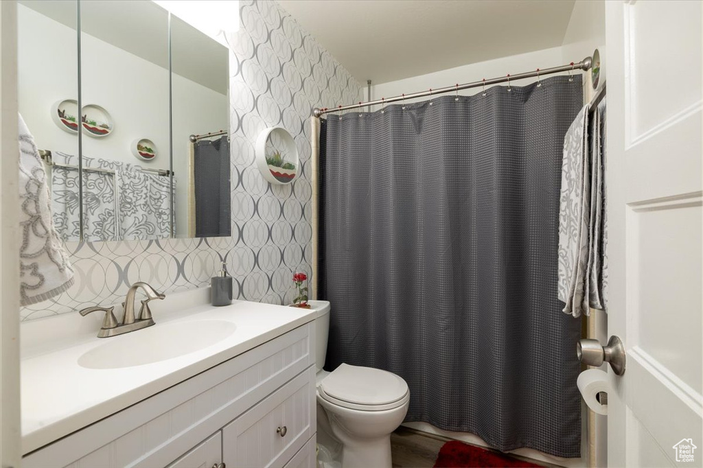 Full bathroom with vanity, wallpapered walls, toilet, and a shower with shower curtain