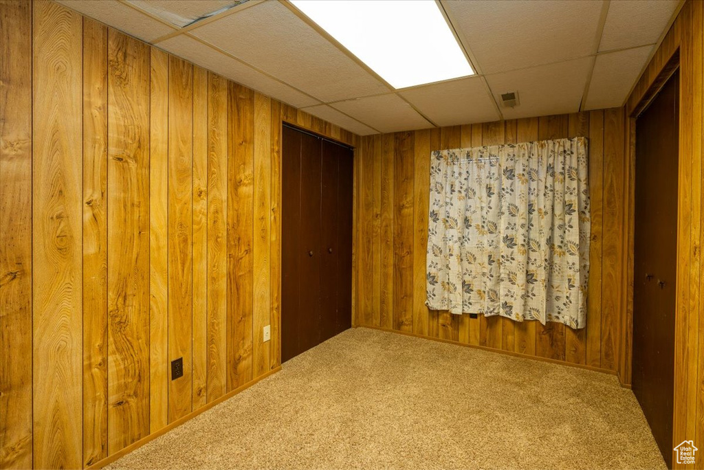 Empty room featuring a paneled ceiling, carpet floors, and wooden walls