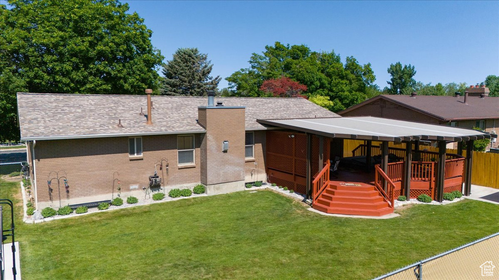 Rear view of property featuring brick siding, a wooden deck, a shingled roof, and a chimney