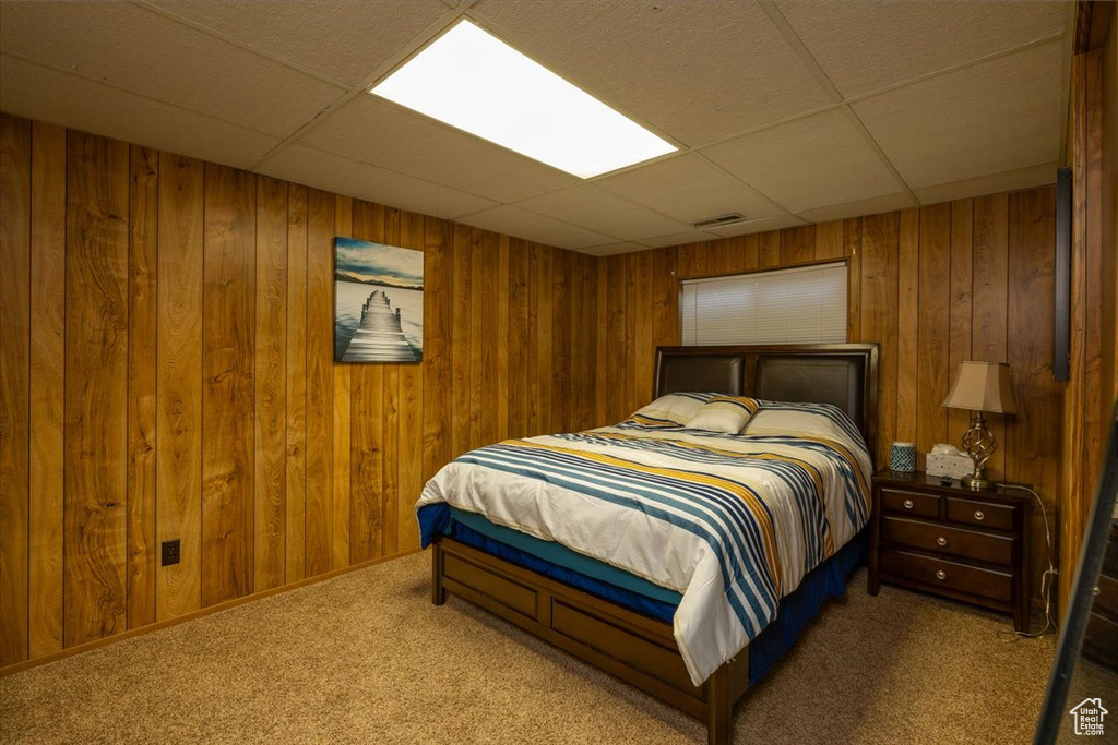 Carpeted bedroom featuring a drop ceiling and wooden walls