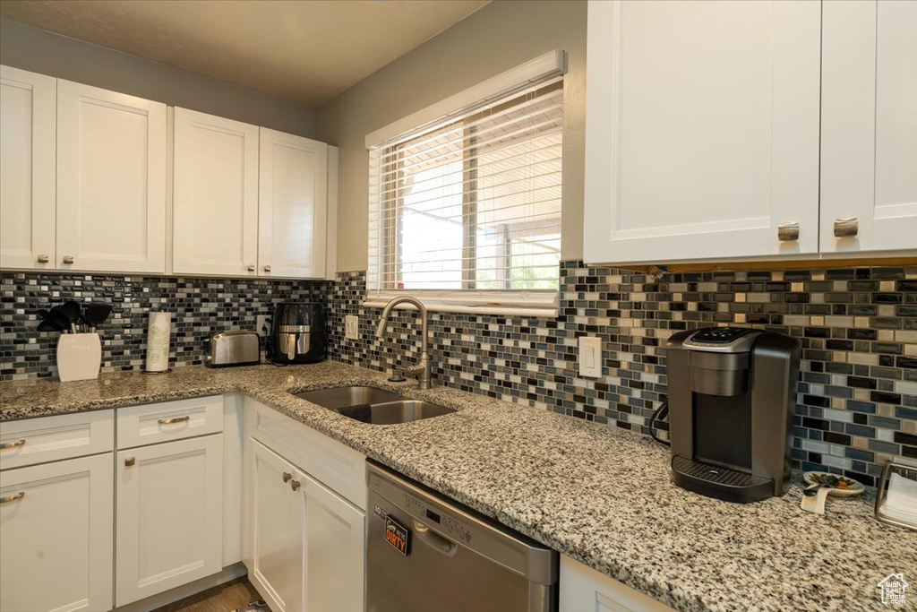 Kitchen with dishwasher, a sink, white cabinets, and decorative backsplash