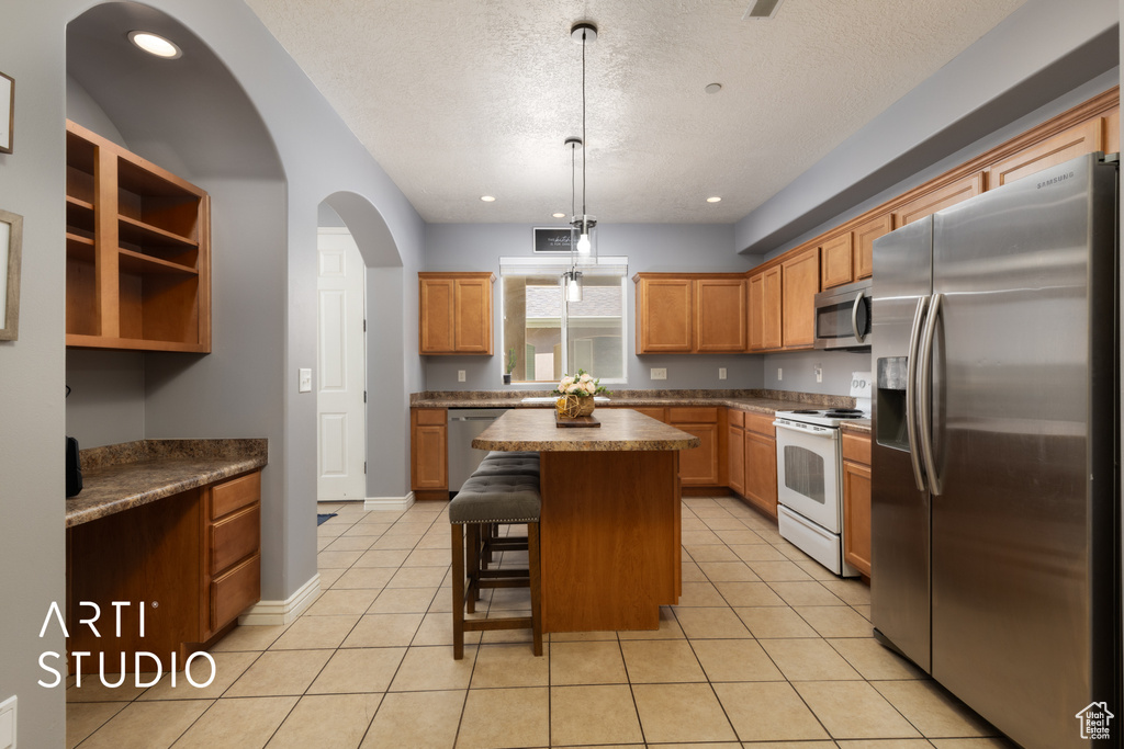 Kitchen featuring stainless steel appliances, a kitchen island, a textured ceiling, a breakfast bar area, and light tile patterned floors