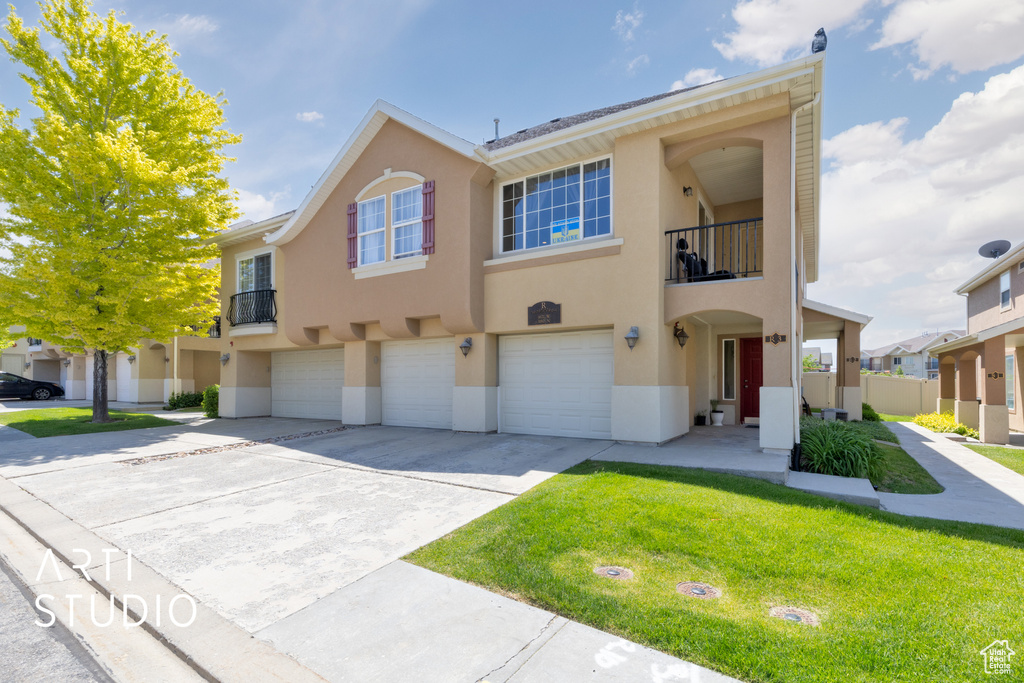 Townhome / multi-family property with a garage, driveway, stucco siding, and a balcony