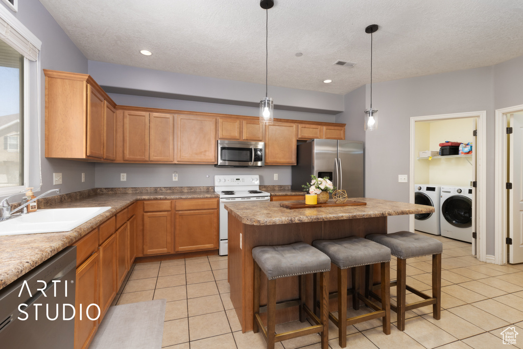 Kitchen featuring stainless steel appliances, washing machine and dryer, a sink, light tile patterned flooring, and a kitchen island