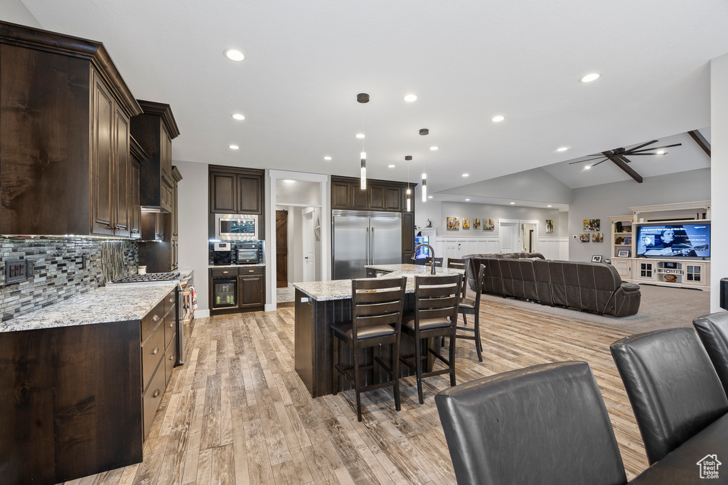Kitchen with built in appliances, open floor plan, dark brown cabinets, a kitchen breakfast bar, and recessed lighting