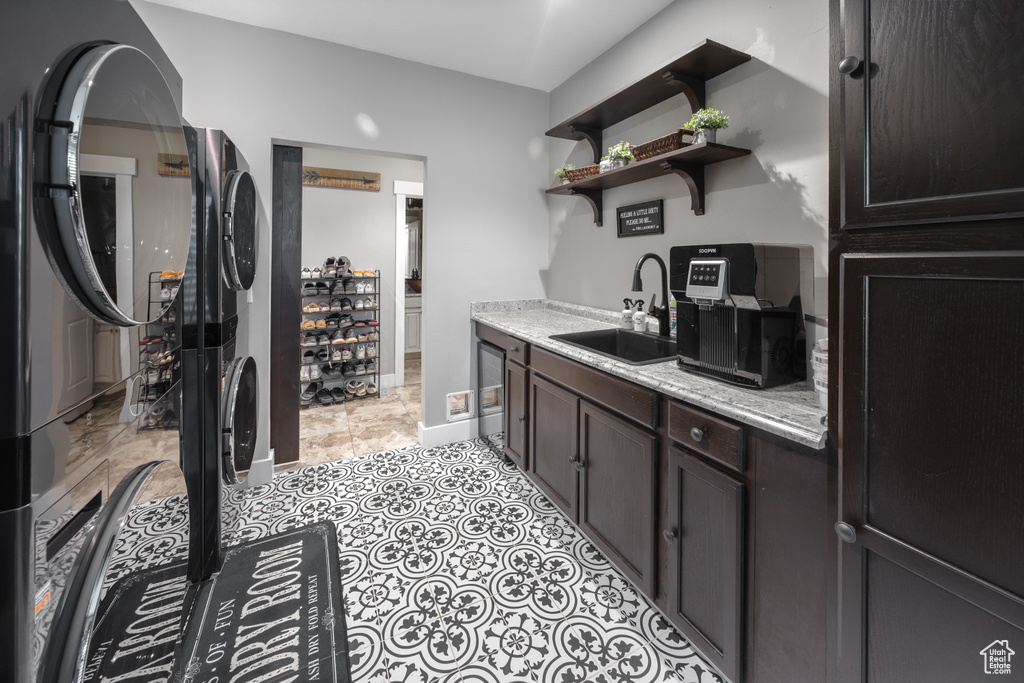 Kitchen featuring a sink, stacked washer / dryer, dark brown cabinets, open shelves, and beverage cooler