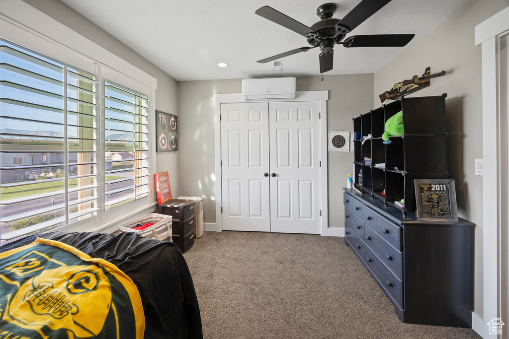 Bedroom with a wall mounted AC, a closet, carpet floors, ceiling fan, and baseboards
