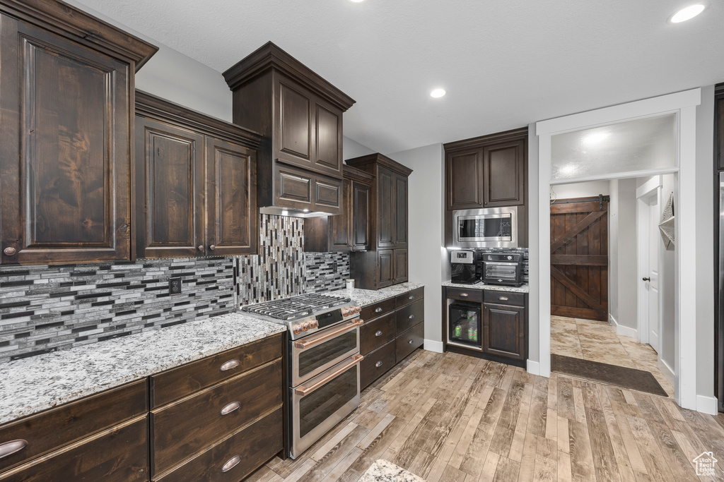 Kitchen with appliances with stainless steel finishes, dark brown cabinets, baseboards, backsplash, and light wood-style flooring