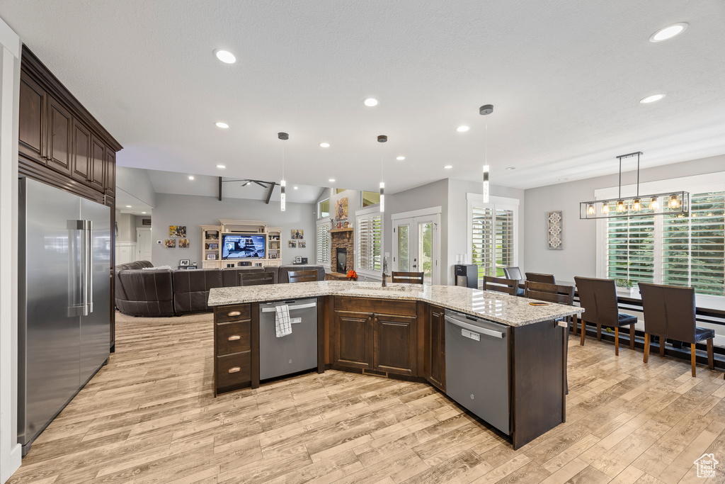 Kitchen with stainless steel appliances, open floor plan, dark brown cabinets, light wood-style floors, and recessed lighting