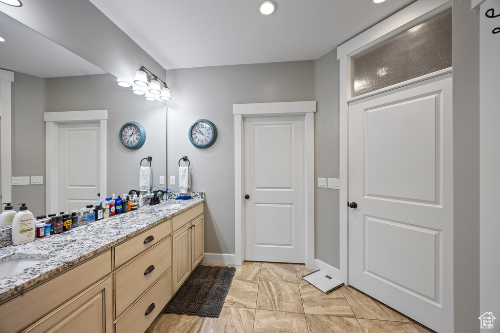 Bathroom featuring double vanity, baseboards, recessed lighting, and marble look tiles