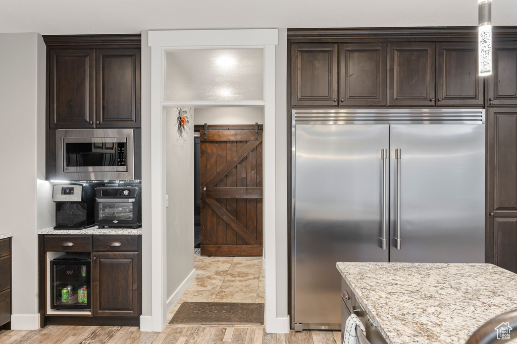 Kitchen featuring built in appliances, dark brown cabinets, and light stone counters