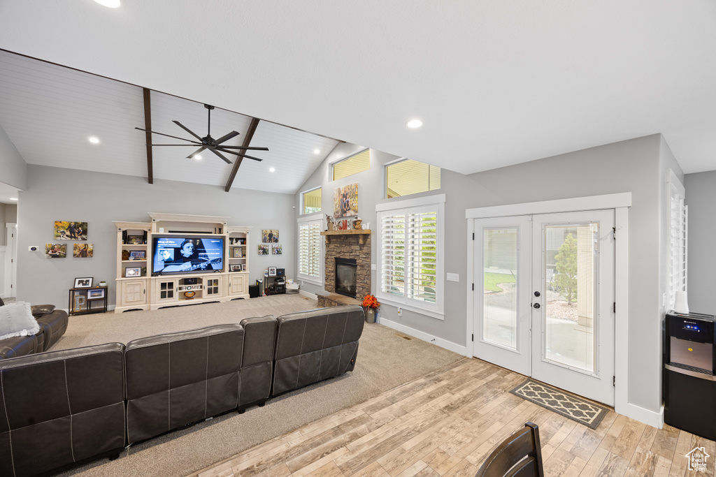 Living area featuring wood finished floors, ceiling fan, baseboards, a stone fireplace, and vaulted ceiling
