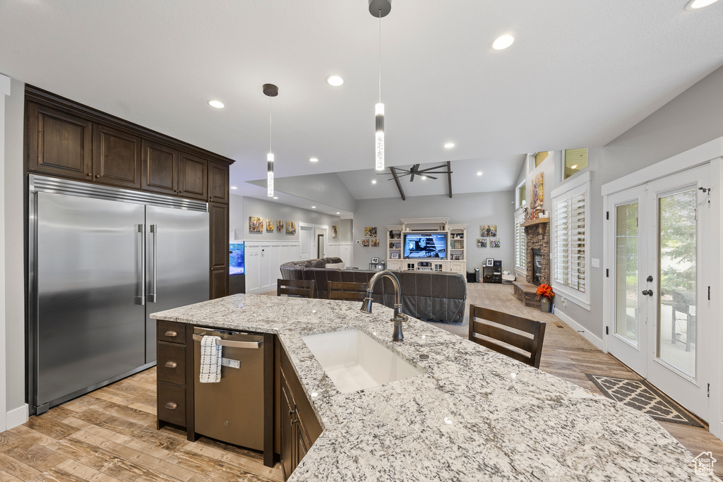 Kitchen with appliances with stainless steel finishes, a sink, dark brown cabinetry, a ceiling fan, and light wood-type flooring