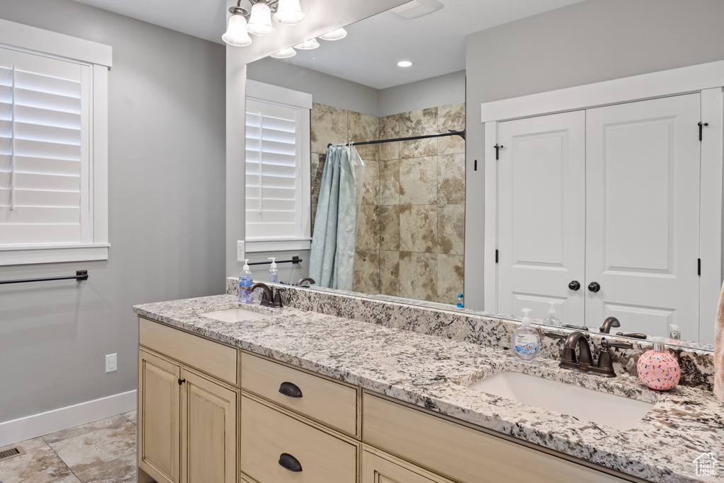 Full bath with double vanity, baseboards, and a tile shower