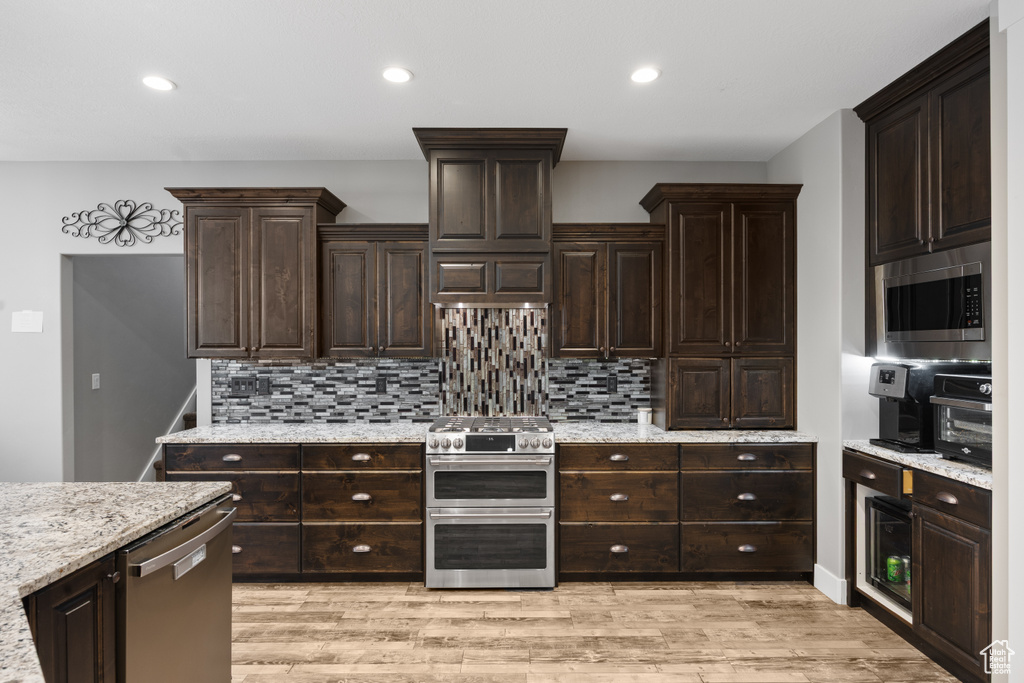Kitchen featuring appliances with stainless steel finishes, decorative backsplash, dark brown cabinetry, light wood-style flooring, and recessed lighting