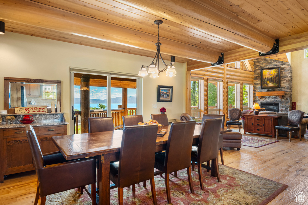 Dining room featuring light wood-style floors, wooden ceiling with exposed beams, a fireplace, and log walls