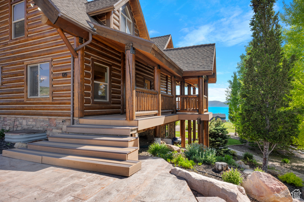 View of property exterior featuring a shingled roof, covered porch, log exterior, and a water view