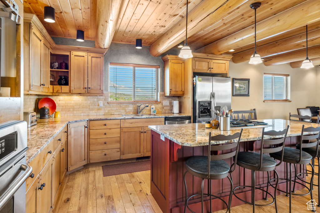 Kitchen featuring appliances with stainless steel finishes, a sink, light wood-type flooring, healthy amount of natural light, and wooden ceiling with exposed beams