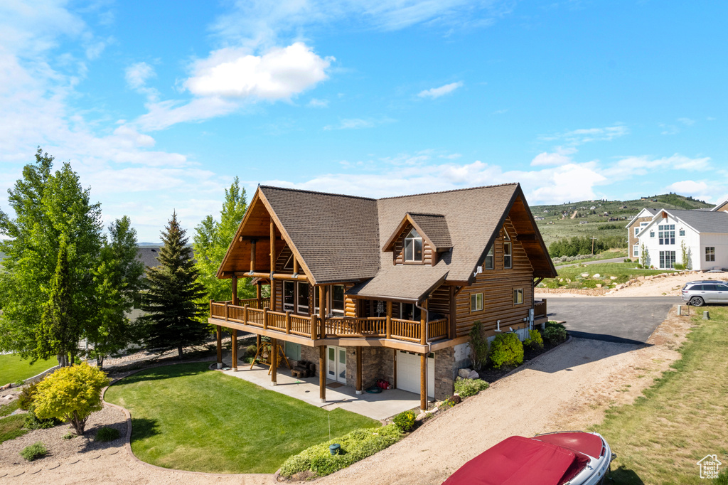 Rear view of house with stone siding, log siding, a yard, dirt driveway, and a deck