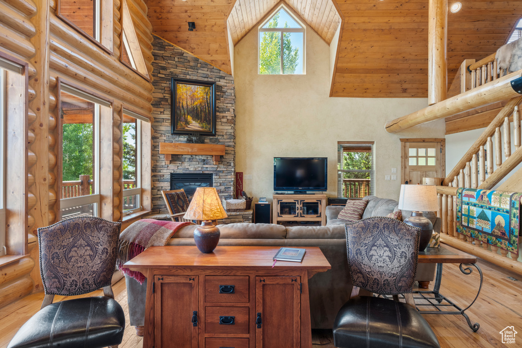 Living area featuring high vaulted ceiling, hardwood / wood-style flooring, wooden ceiling, a stone fireplace, and log walls