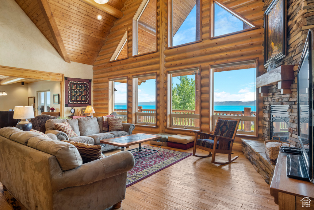 Living room with high vaulted ceiling, log walls, wooden ceiling, a stone fireplace, and light wood-type flooring