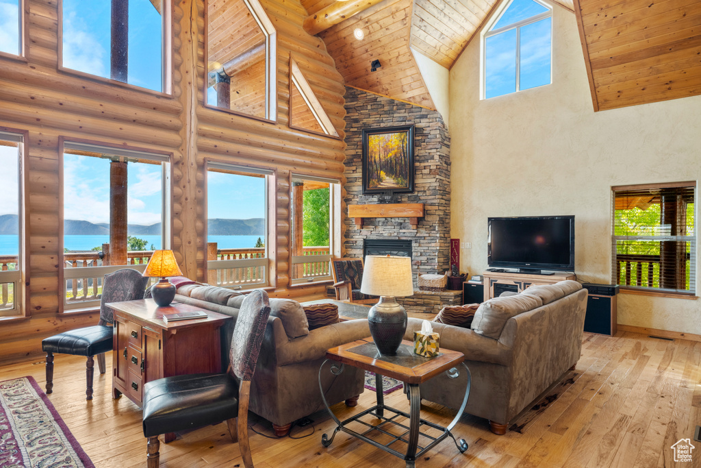 Living area featuring high vaulted ceiling, log walls, a stone fireplace, wood-type flooring, and wooden ceiling