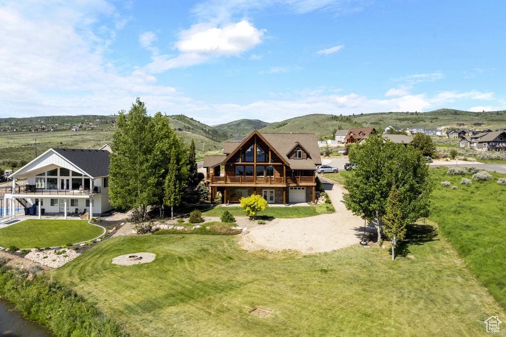 Back of house featuring a garage, a yard, a deck with mountain view, driveway, and stone siding