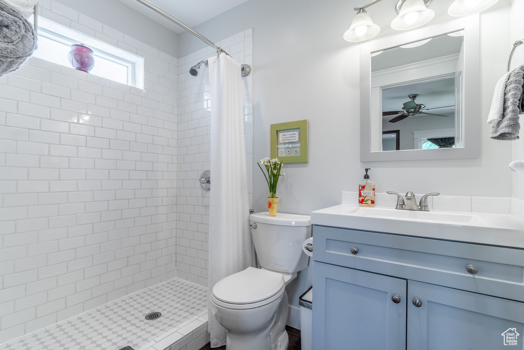 Full bath featuring toilet, vanity, tiled shower, and ceiling fan
