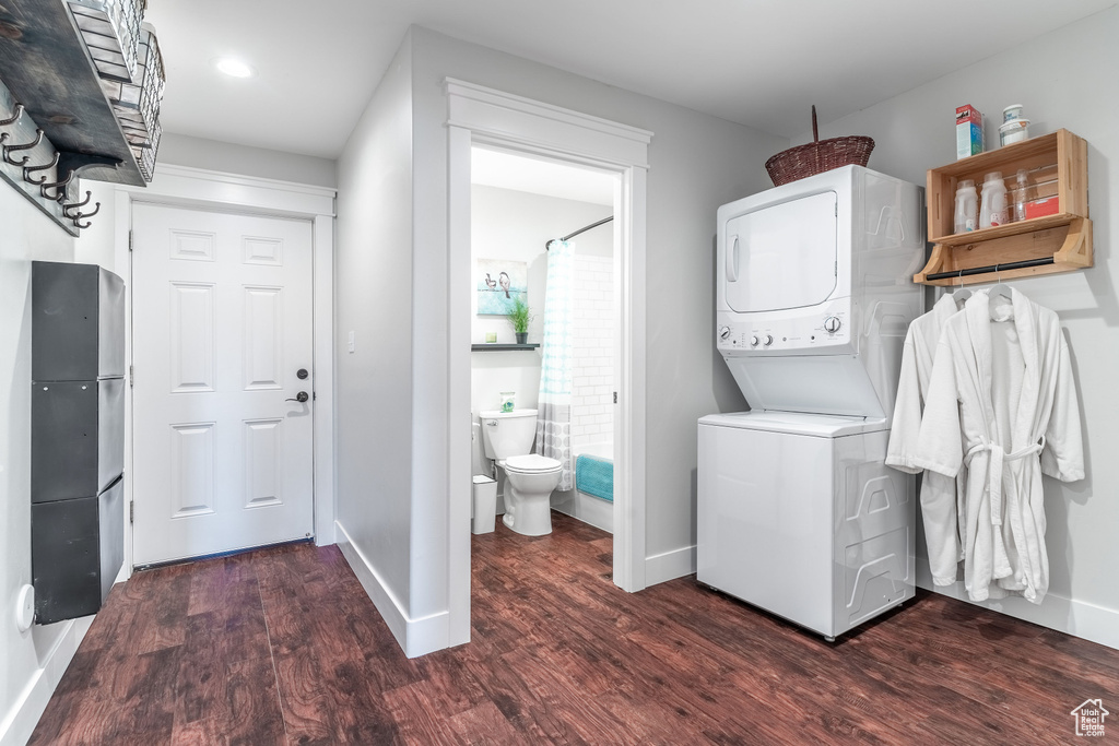 Washroom with stacked washing machine and dryer, wood finished floors, baseboards, and recessed lighting