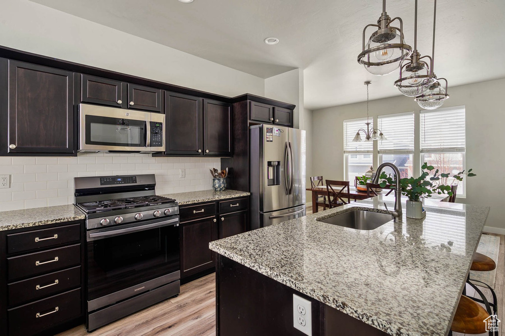 Kitchen featuring appliances with stainless steel finishes, a sink, backsplash, light wood finished floors, and a kitchen bar