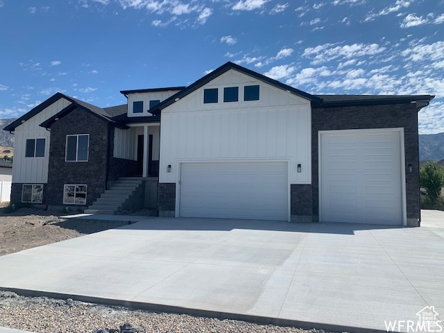View of front facade with stone siding, an attached garage, board and batten siding, and concrete driveway