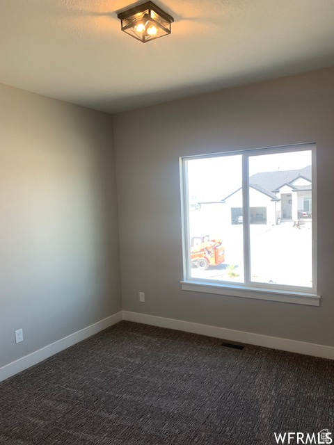 Empty room featuring baseboards and dark carpet