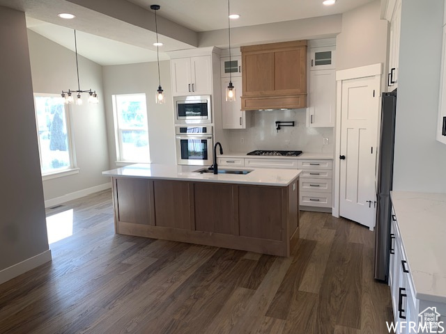 Kitchen with appliances with stainless steel finishes, dark wood finished floors, tasteful backsplash, a sink, and baseboards