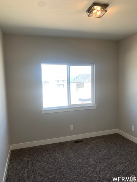 Empty room featuring dark carpet, plenty of natural light, and baseboards
