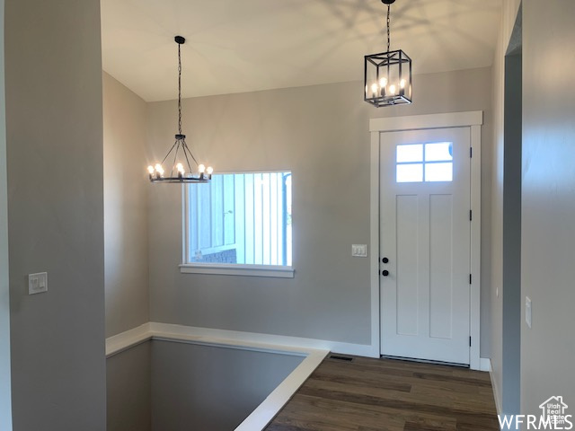 Entrance foyer with a chandelier, dark wood-type flooring, and baseboards