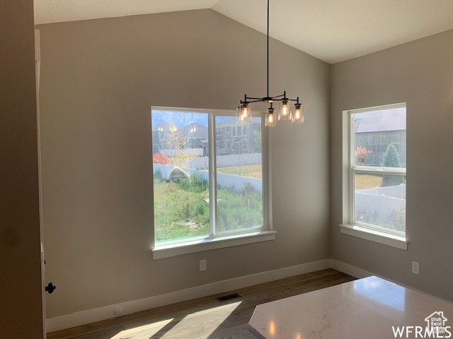Unfurnished dining area featuring a chandelier, plenty of natural light, wood finished floors, lofted ceiling, and baseboards