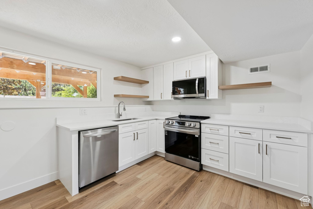Kitchen featuring open shelves, stainless steel appliances, a sink, white cabinets, and recessed lighting