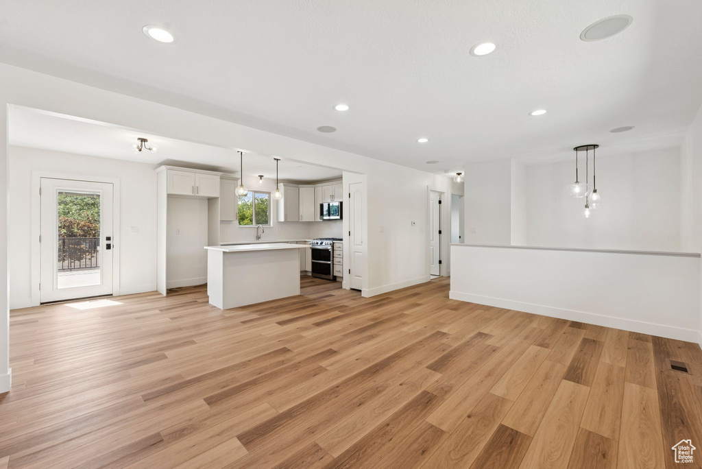 Unfurnished living room with healthy amount of natural light, light wood-type flooring, recessed lighting, and baseboards