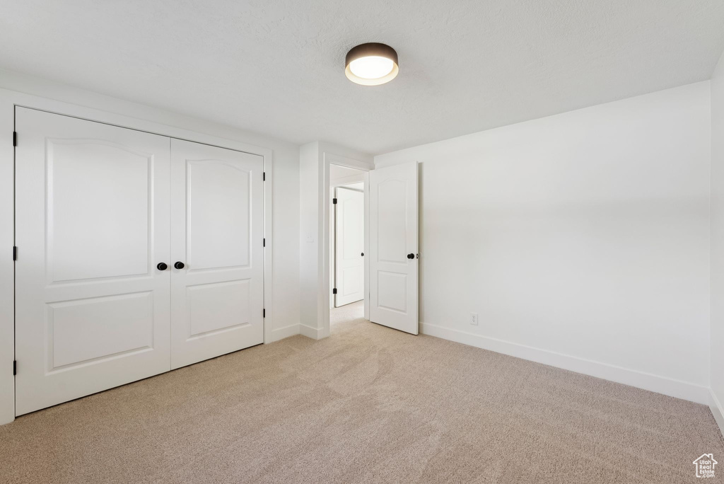 Unfurnished bedroom featuring light carpet, baseboards, and a closet