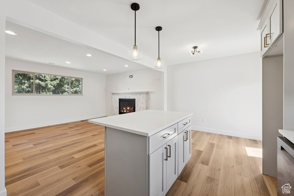 Kitchen with a lit fireplace, light wood-type flooring, light countertops, pendant lighting, and recessed lighting