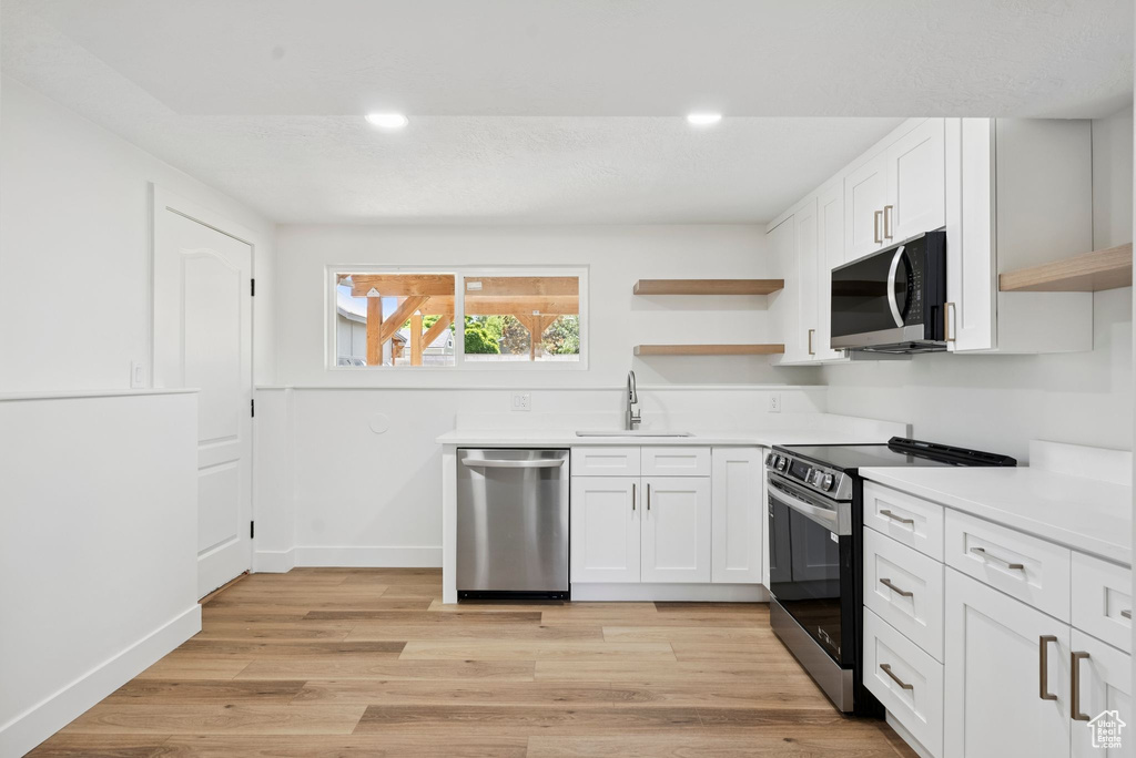 Kitchen with open shelves, stainless steel appliances, a sink, white cabinetry, and light countertops
