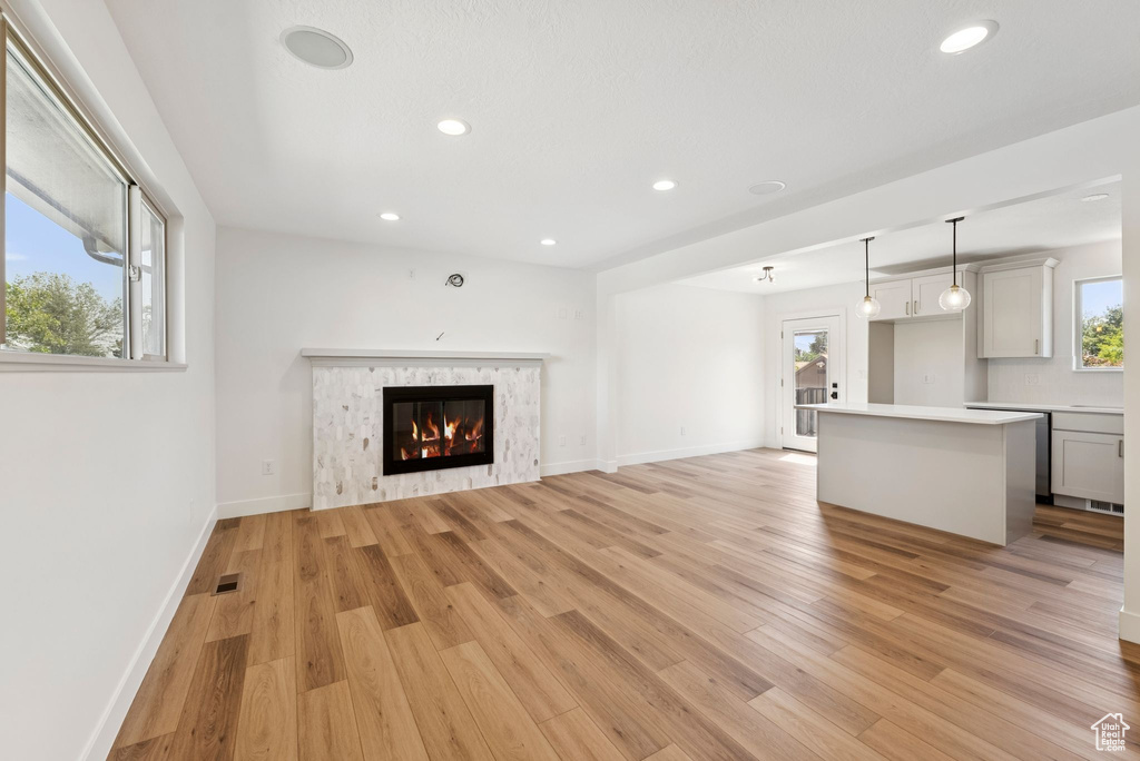 Unfurnished living room with light wood-type flooring, healthy amount of natural light, recessed lighting, and a glass covered fireplace