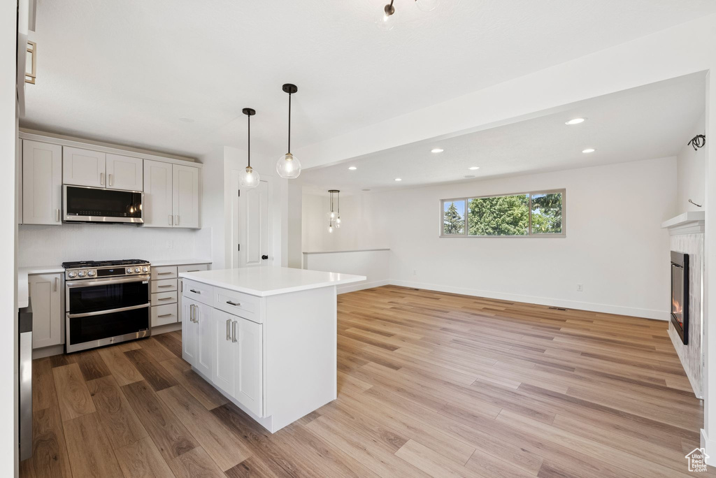 Kitchen with stainless steel appliances, light wood-style flooring, recessed lighting, light countertops, and a glass covered fireplace