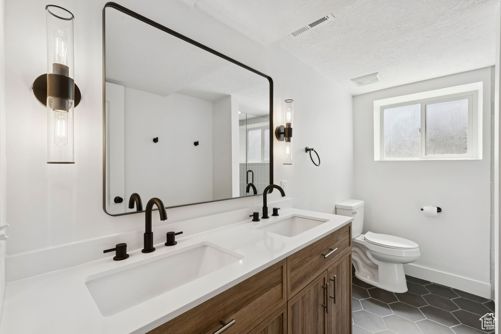 Full bath featuring double vanity, toilet, tile patterned floors, and baseboards