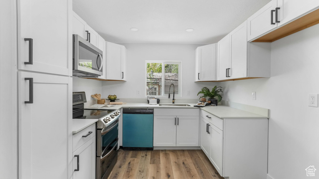 Kitchen with appliances with stainless steel finishes, a sink, light wood finished floors, white cabinetry, and recessed lighting
