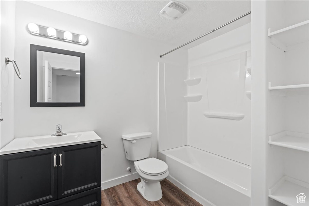 Bathroom featuring vanity, wood finished floors, toilet, a textured ceiling, and bathing tub / shower combination